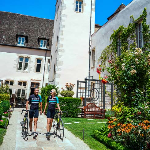 Two cyclists walking their bikes in the courtyard of Le Cep hotel in Beaune