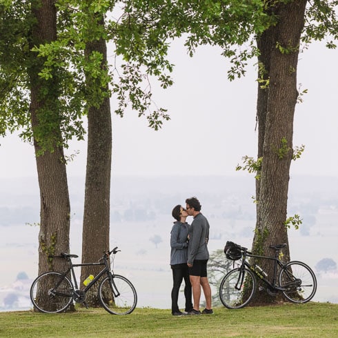 Couple kissing with their bikes leaned against oak trees on a DuVine cycling tour of Bordeaux